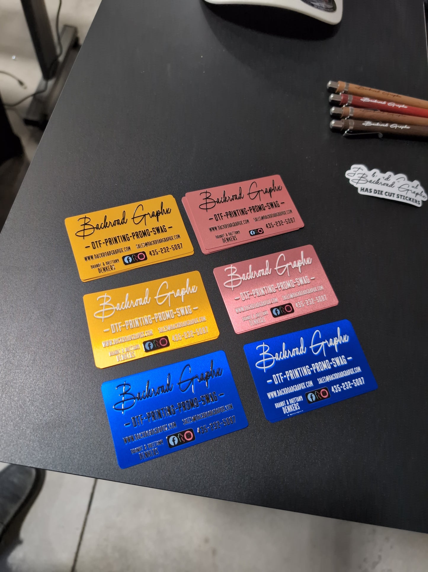 Colorful business cards on a dark surface with pencils and a white object.